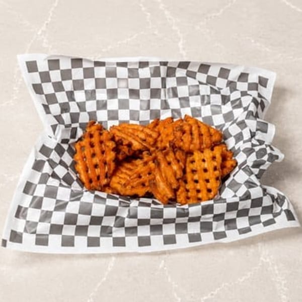 Golden waffle fries in a black and white checkered paper liner on a light stone surface.