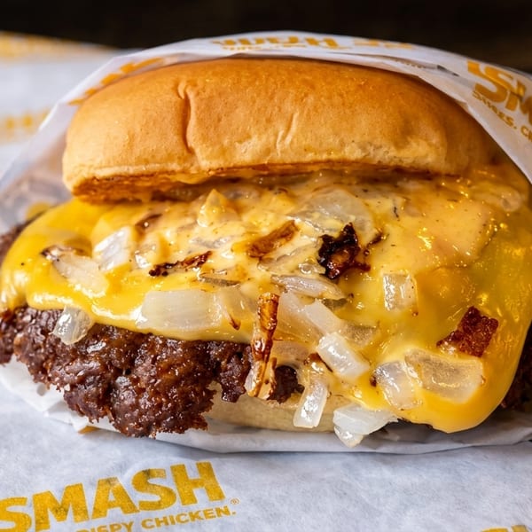 A Smashburger with melted cheese and grilled onions, wrapped in branded paper.