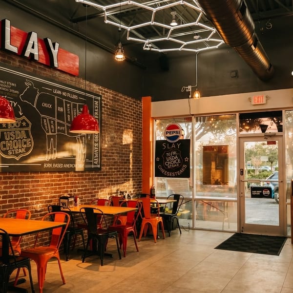 Interior of Slay Steak restaurant with brick walls, red chairs, and a large steak cut diagram.