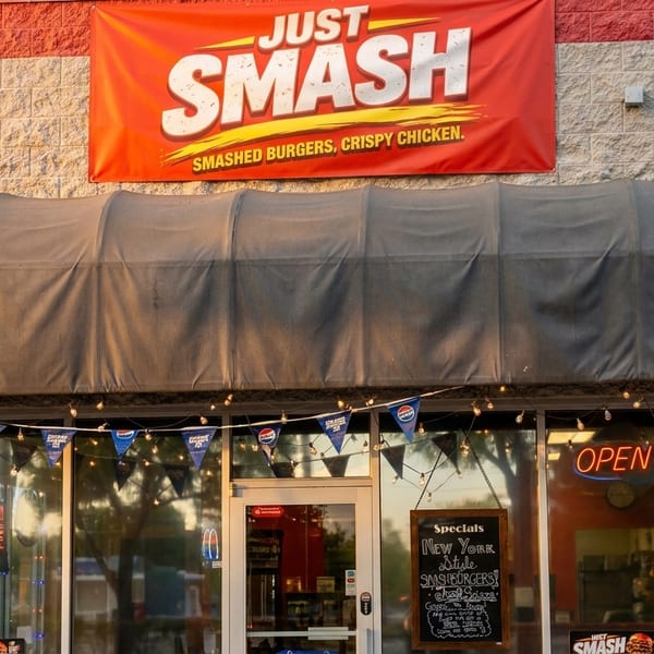 Exterior of Just Smash restaurant with a red banner, gray awning, and "OPEN" sign in the window.
