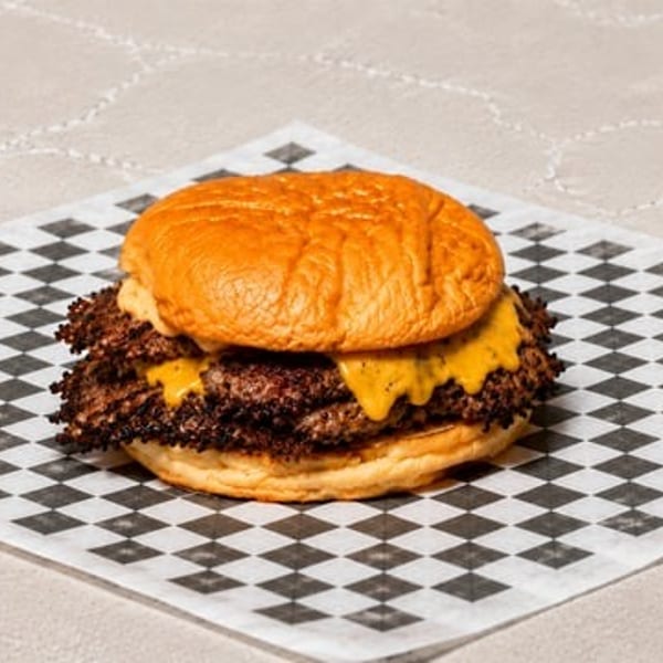 Double smash burger with melted cheese on a brioche bun, served on checkered paper.
