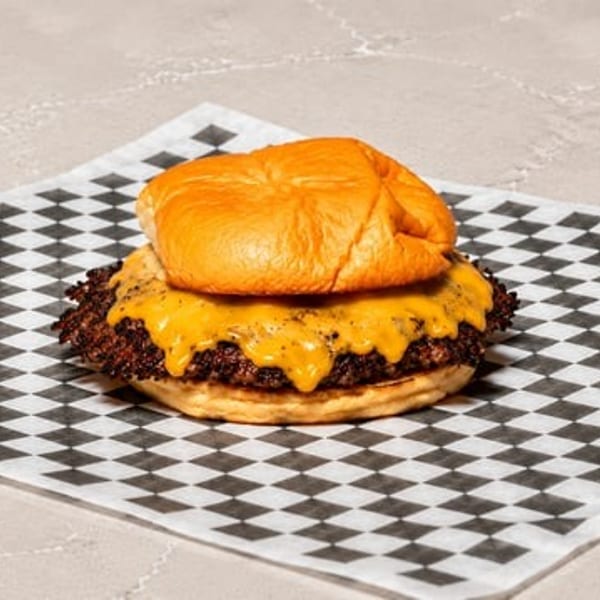 Cheesy smash burger with a golden bun on black and white checkered paper.