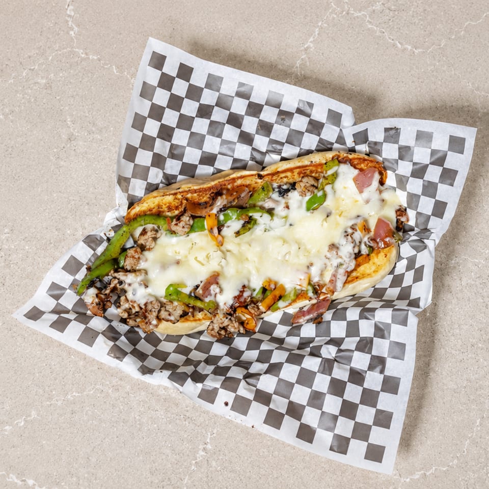 A cheesesteak sandwich with melted cheese, green peppers, and onions on checkered paper.