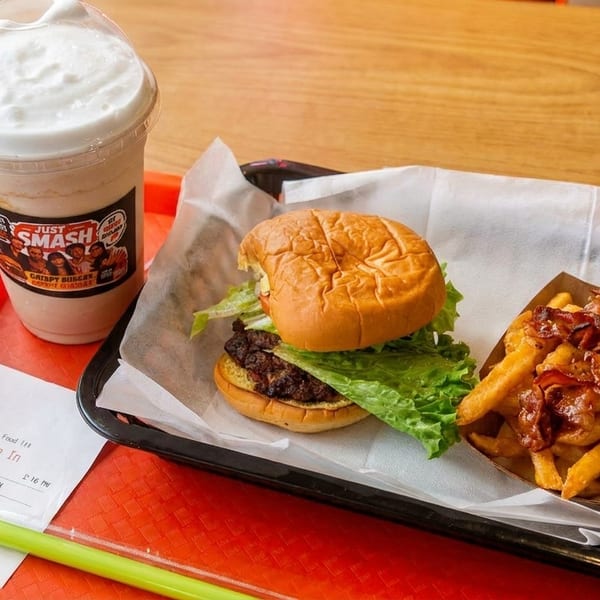 A Smashburger meal with a burger, bacon cheese fries, and a milkshake on a red tray.