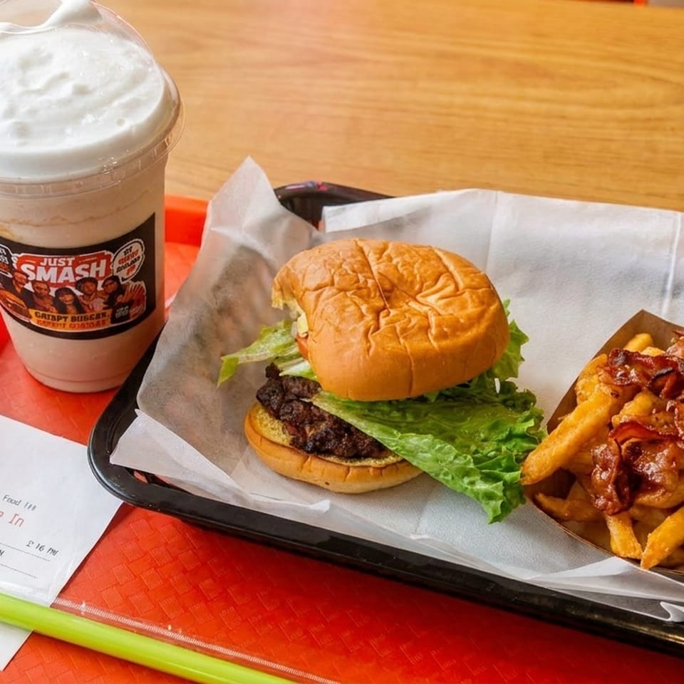 A Smashburger meal with a burger, bacon cheese fries, and a milkshake on a red tray.