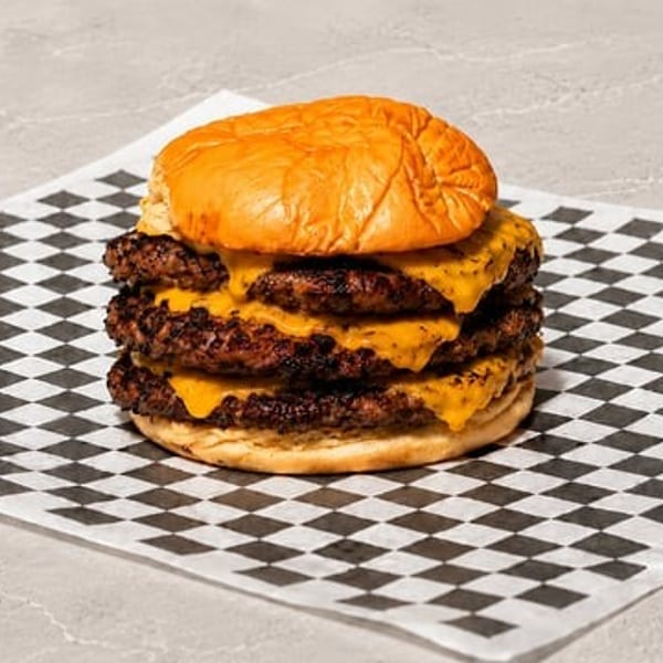 Triple cheeseburger with melted cheese on a toasted bun, resting on checkered paper.