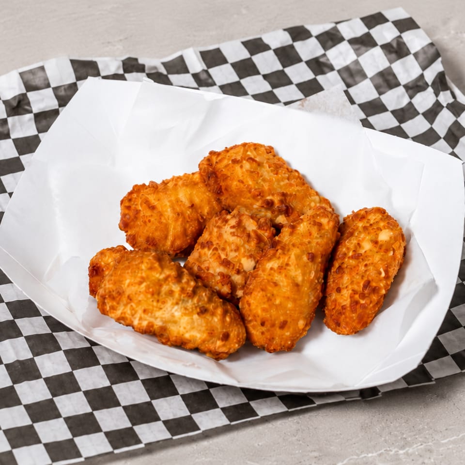 Crispy golden fried food pieces in a white paper boat on a black and white checkered liner.