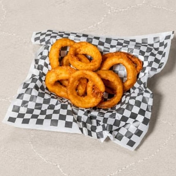 A serving of crispy golden onion rings in a checkered paper basket.
