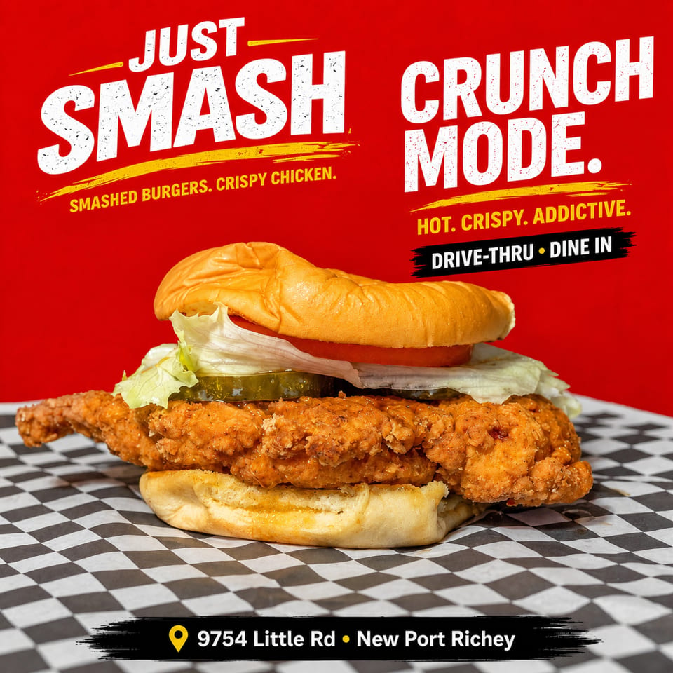 Crispy chicken sandwich with lettuce, tomato, pickles, and sauce on checkered paper beneath bold restaurant advertising.