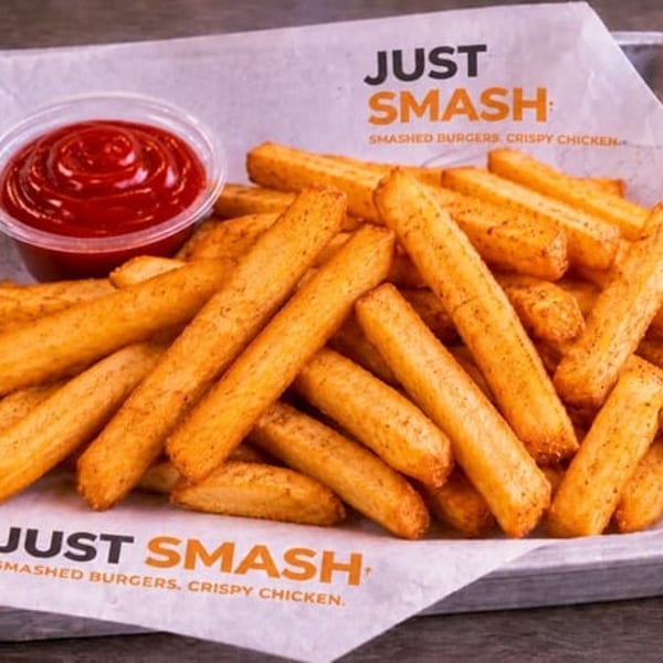 Golden french fries with ketchup in a metal tray, on "Just Smash" branded paper.